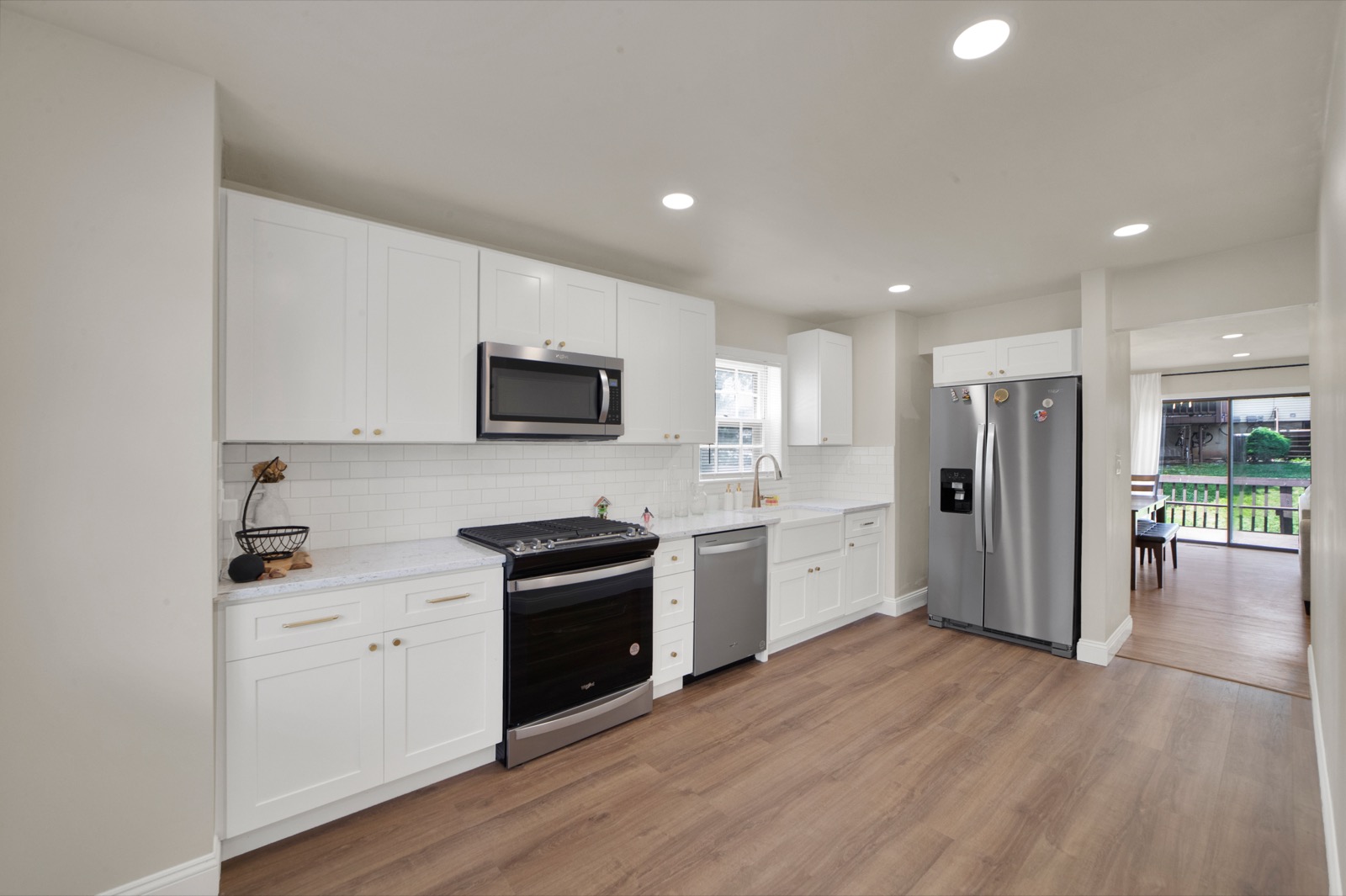 A finished kitchen renovation by Garden State ADU: white shaker cabinets, quartz counters, subway-tile backsplash, stainless appliances, and luxury vinyl plank flooring opening to a backyard.